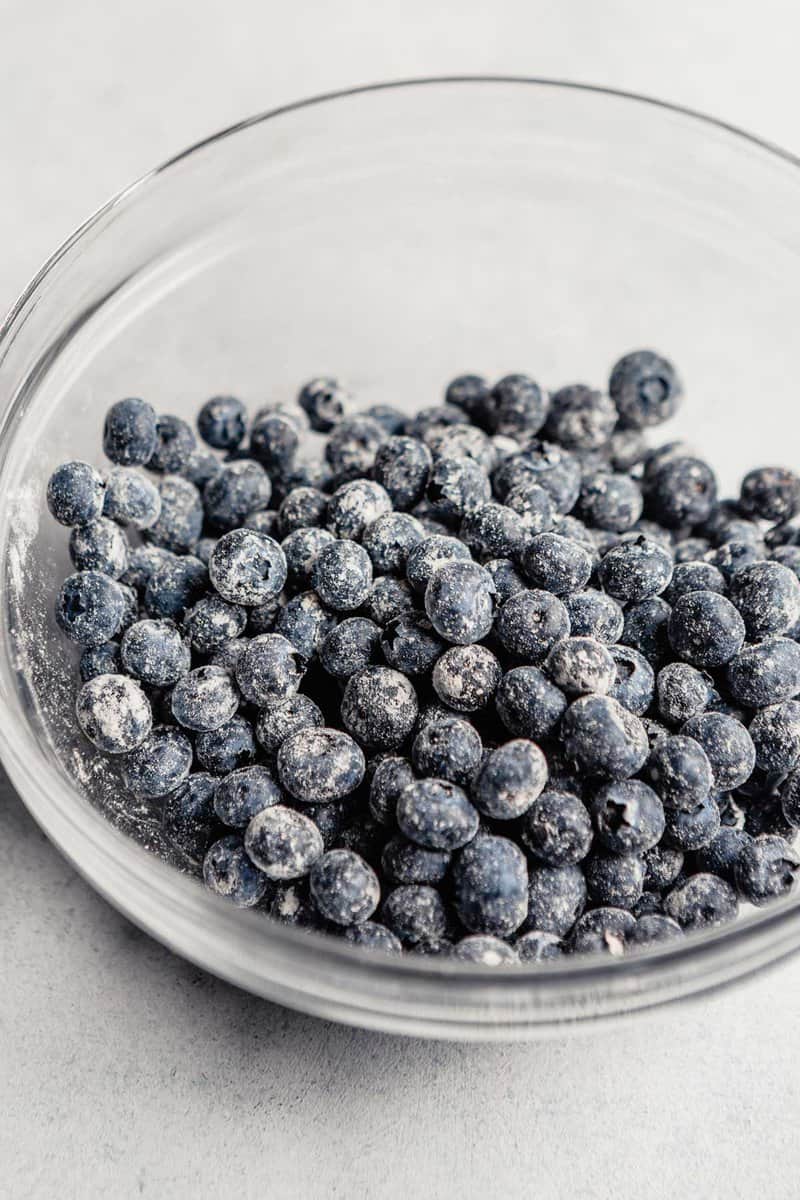 Fresh blueberries coated in a light dusting of flour in a glass mixing bowl.