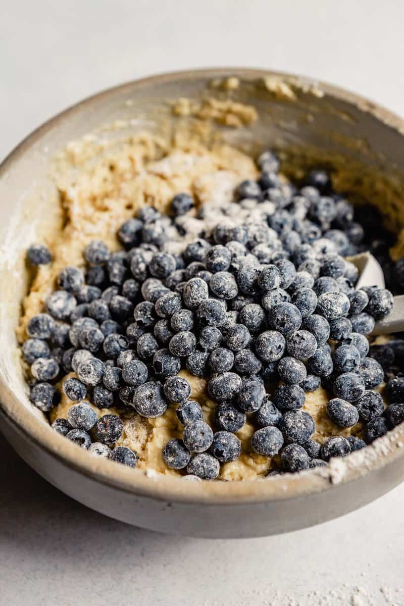 Blueberries coated in flour poured over top a bowl full of muffin batter.