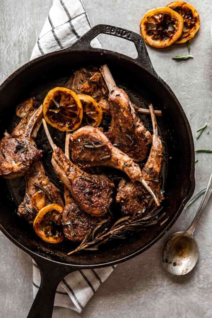 Overhead image of lamb chops in a cast-iron skillet set on top of a stripped towel with a spoon set to the side