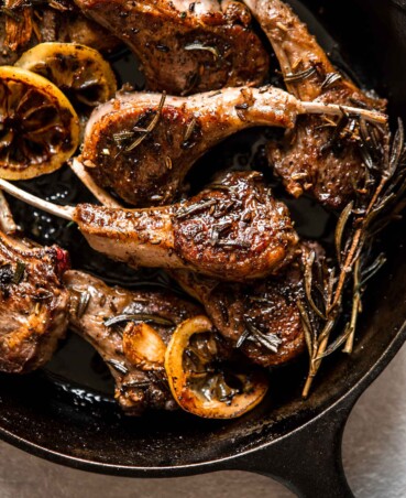 Overhead image of lamb chops in a cast-iron skillet set on top of a stripped towel with a spoon set to the side