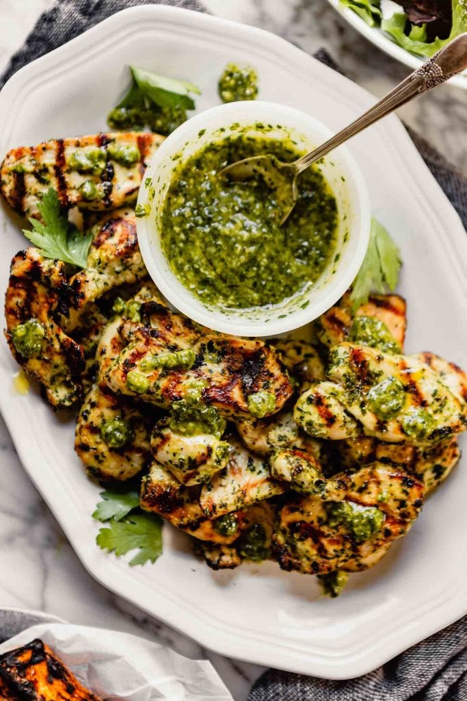 grilled chimichurri chicken breast one a white plate with a bowl of chimichurri set off to the side