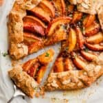 peach galette set on a piece or parchment paper with a slice being taken out