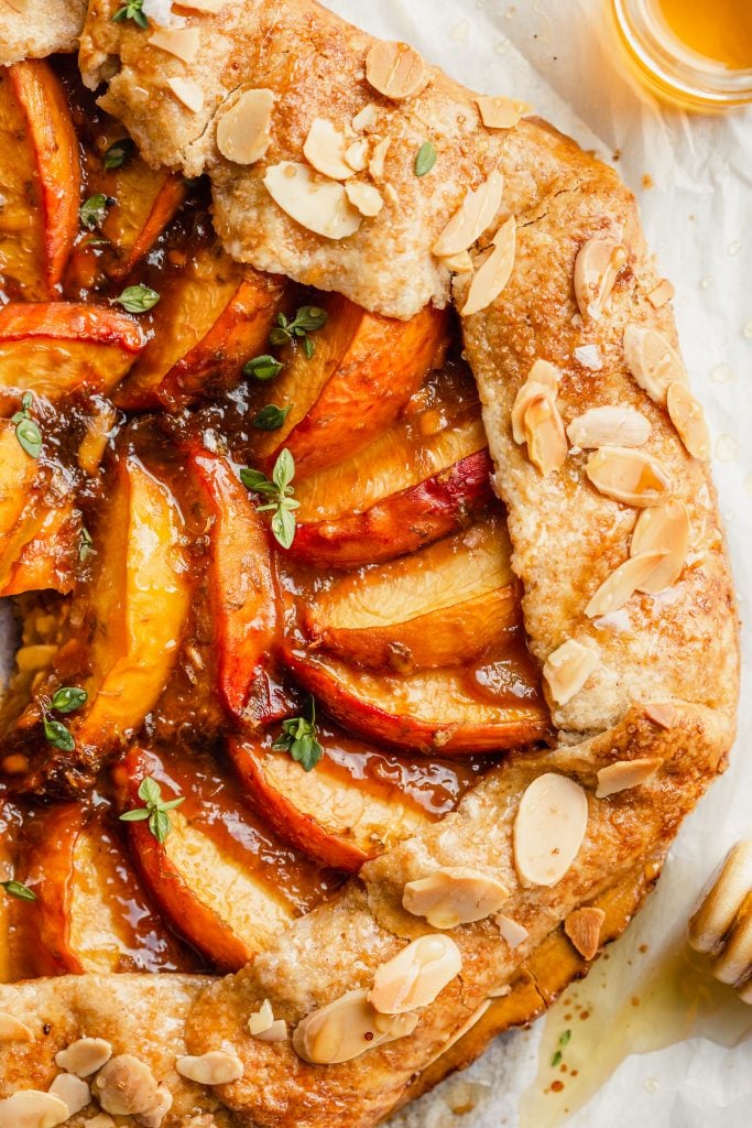 peach galette set on a piece or parchment paper with a slice being taken out