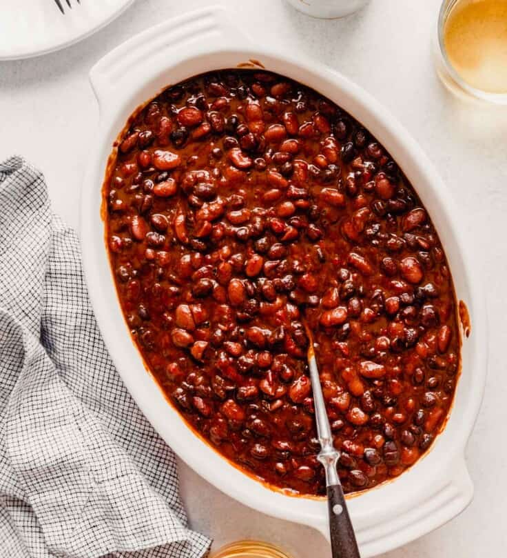 baked beans in a white oval dish with a spoon in them