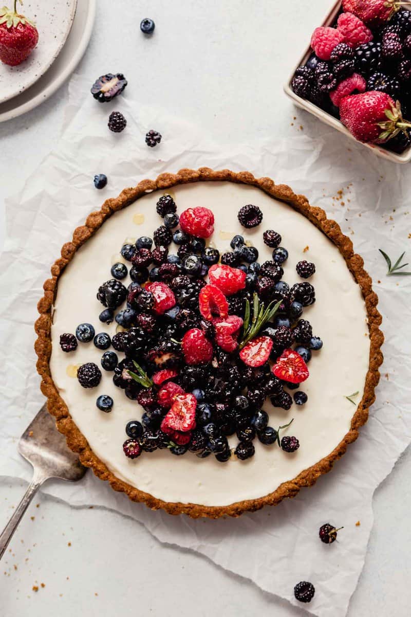 tart set on parchment paper with berries scattered around