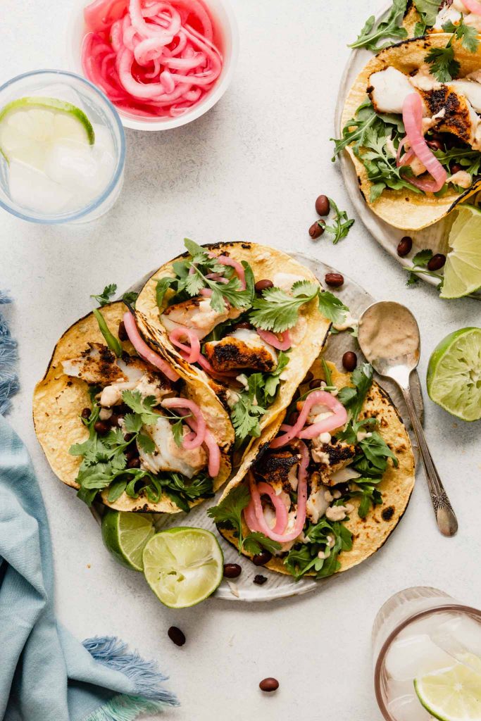 tacos arranged on a flat white plate topped with pickled onions, black beans and arugula