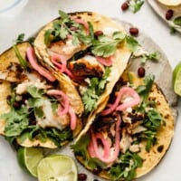 three corn tortillas filled with flaked blackened fish, arugula, a creamy sauce, black beans and pickled onions