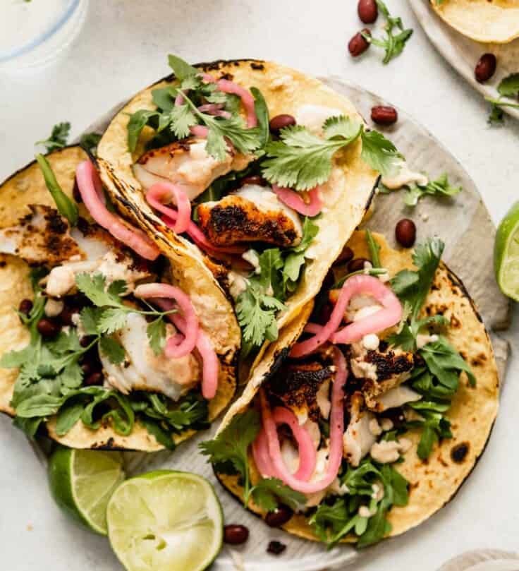 three corn tortillas filled with flaked blackened fish, arugula, a creamy sauce, black beans and pickled onions