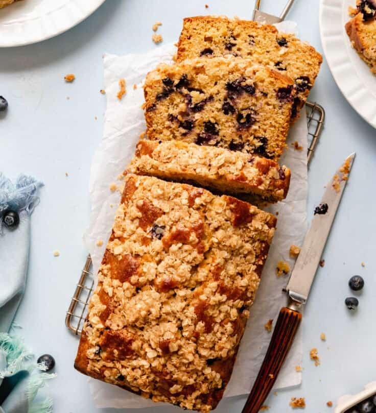lemon blueberry bread on a wire rack set on a blue countertop with a knife set off to the side