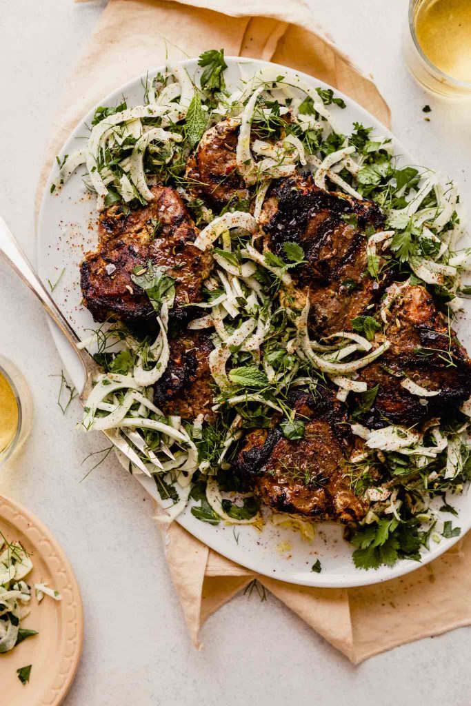 grilled lamb chops arranges over thinly sliced fennel on a white plate