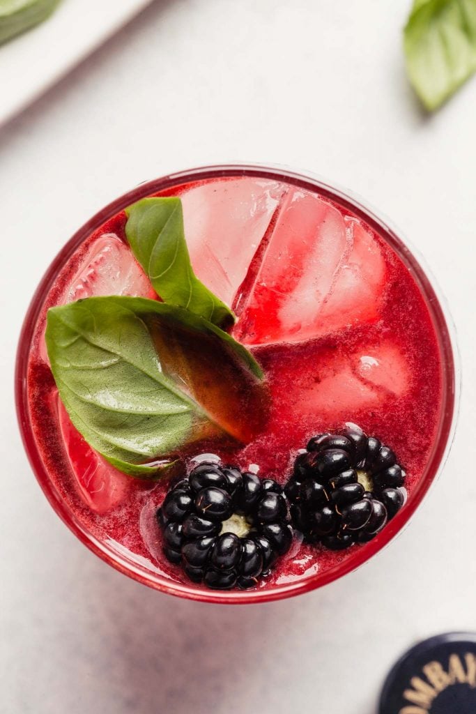 pink cocktail in a tall glass topped with blackberries and basil leaves