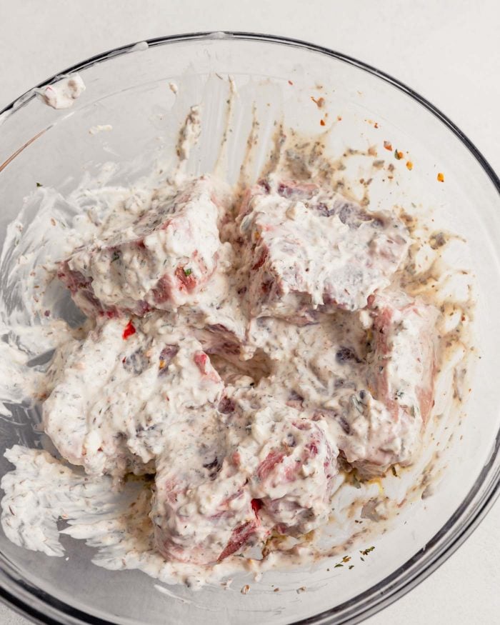 lamb chops covered in a yogurt marinade in a glass bowl