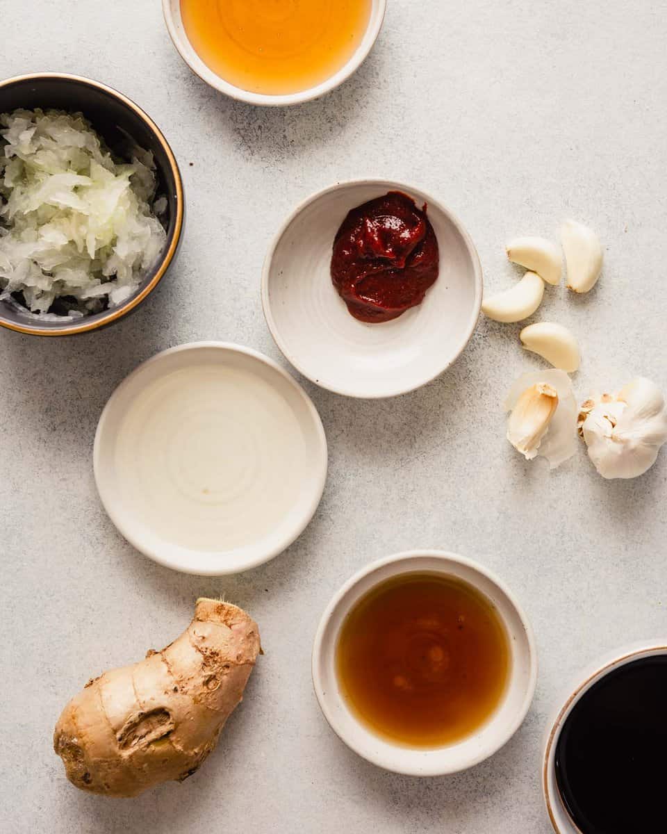 small white bowls filled with ingredients for the bulgogi marinade—soy sauce, grated onion, ginger, honey, mirin, gochujang, sesame oil, gallic cloves