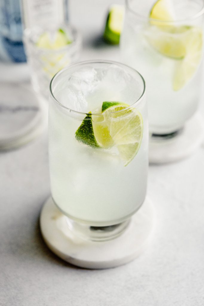 tall glass filled with ice, clear liquid, and lime wedges
