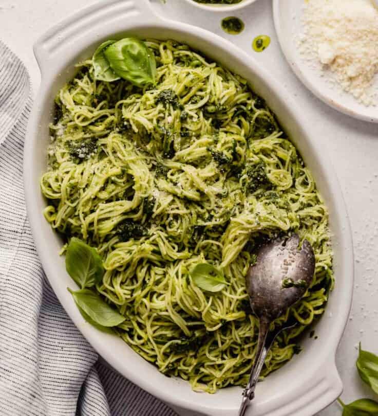 pesto noodles in a white oval dish with cheese and pesto set around