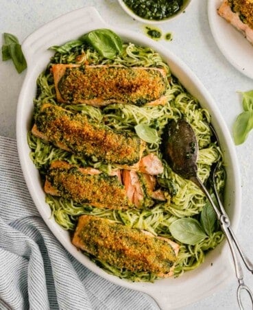 pesto pasta in a white baking dish topped with breaded salmon fillets