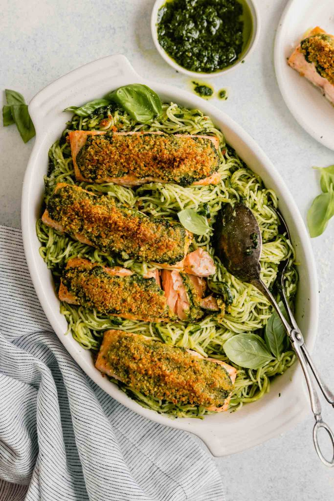 pesto pasta in a white baking dish topped with breaded salmon fillets