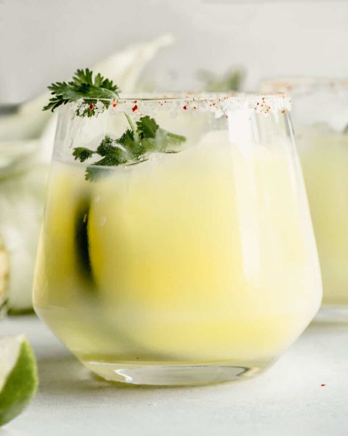 cocktail glass filled with a creamy yellow cocktail and garnished with cilantro.