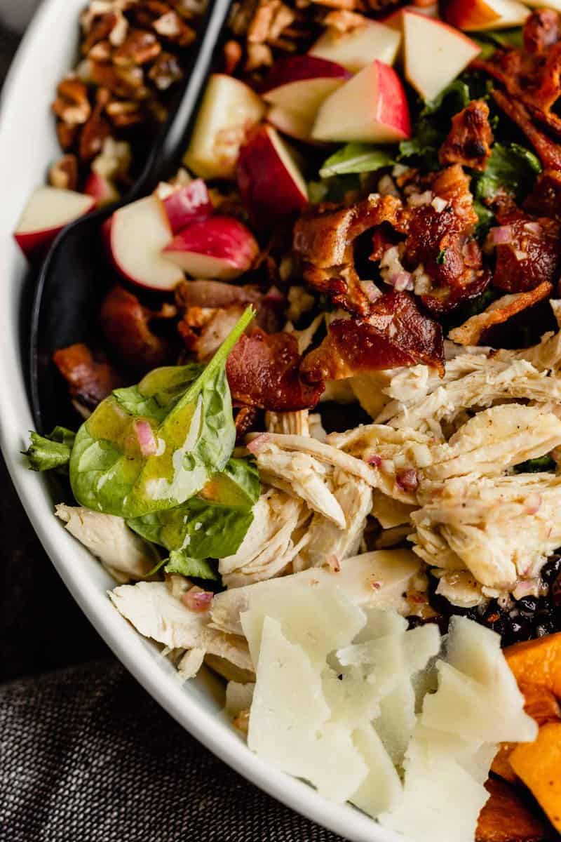 close up of lettuce with maple vinaigrette on it alongside shreds of cheese, shreds of turkey, crisp bits of bacon, diced apple and chopped pecans. A harvest cobb salad!