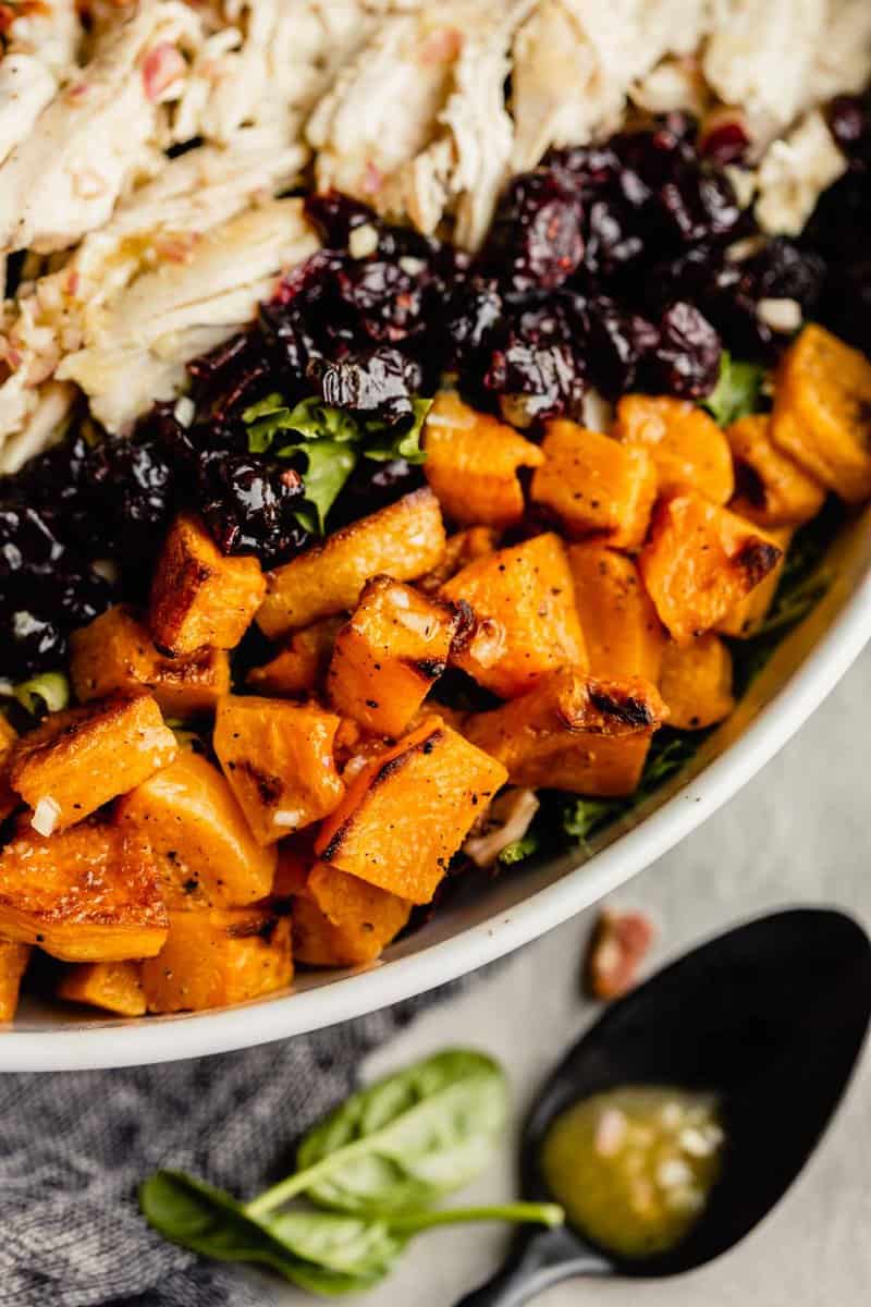 close up of roasted butternut squash in a white bowl filled with lettuce, chicken and cranberries
