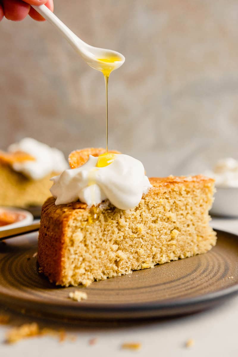 Olive oil being drizzled over a dollop of whipped cream on top of a slice of cake