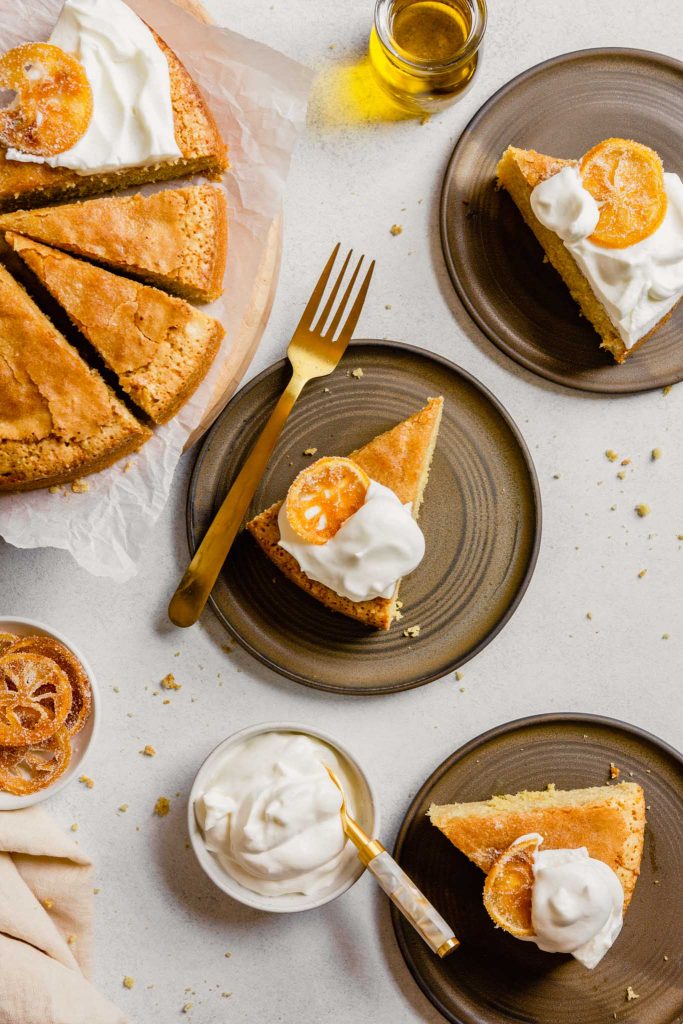 Slices of cake on brown plates topped with whipped cream and candied citrus