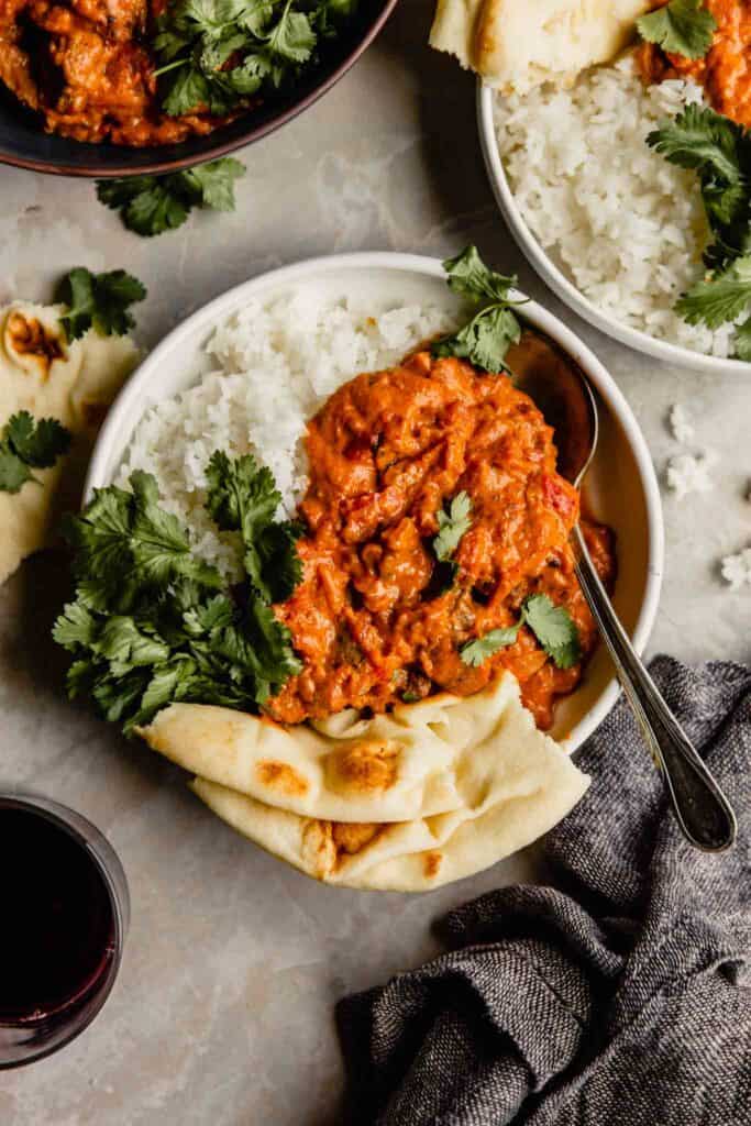 Creamy red sauce over white rice in a bowl with naan bread and cilantro