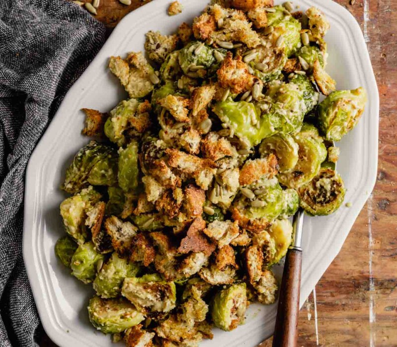 roasted brussels sprout salad on a white oval plate set on a messy wooden table
