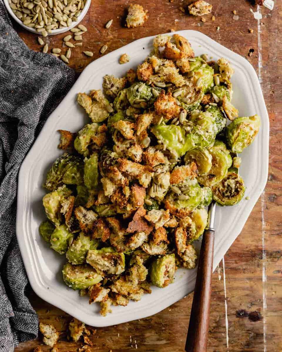 roasted brussels sprout salad on a white oval plate set on a messy wooden table