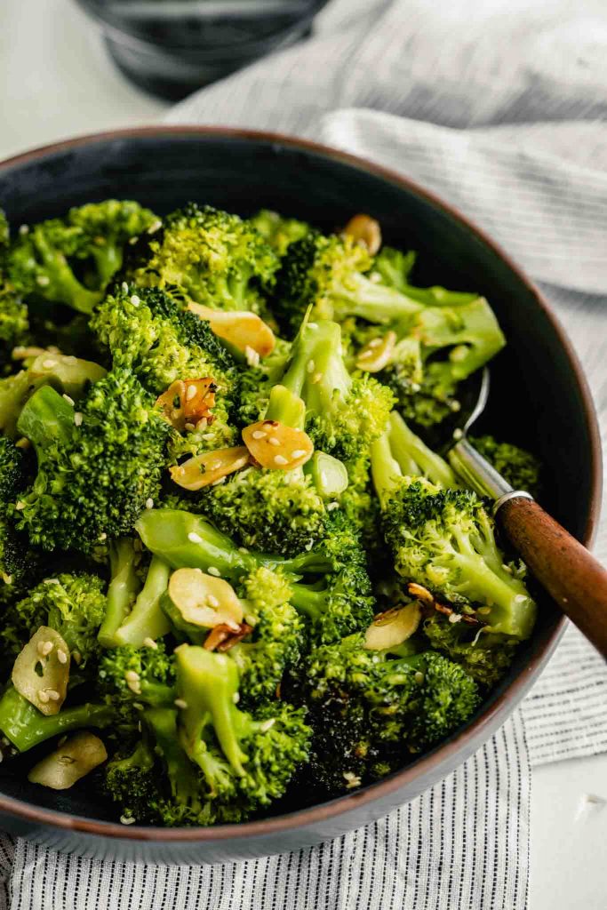 sauteed broccoli in a white bowl with a wooden spoon