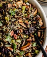 wild rice stuffing in a white oval baking dish set on a wood board on a gray table