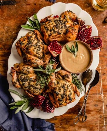herby-roasted cornish hens on a white platter with herbs and pomegranate pieces