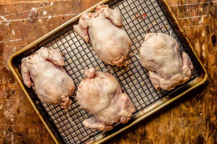 cornish hens on a wire rack set inside a baking sheet