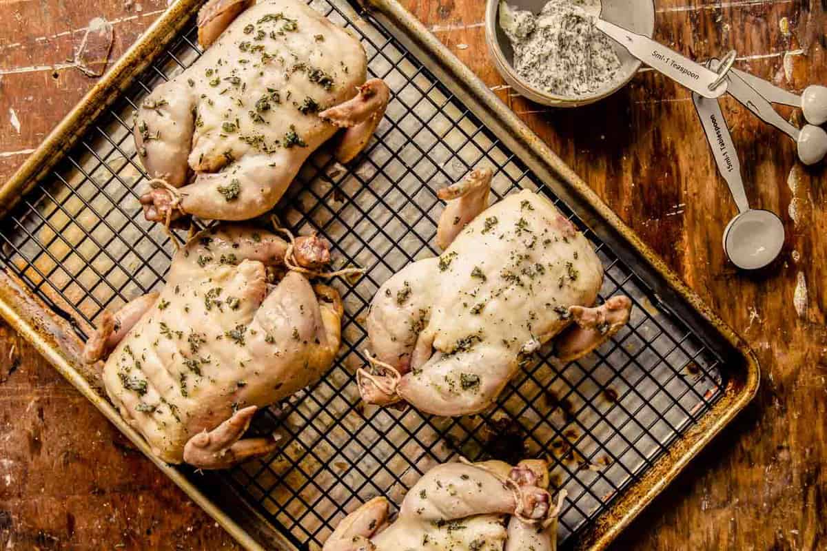 butter and herb-coated cornish hens on a wire rack set inside a baking sheet
