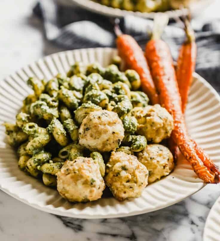 chicken meatballs on a plate with pesto pasta and roasted carrots