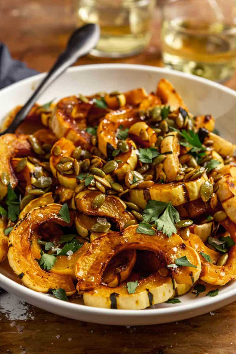 roasted delicata squash slices in a white bowl topped with pepitas, parsley and flaky sea salt.