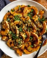 roasted delicata squash slices in a white bowl topped with pepitas, parsley and flaky sea salt.