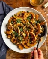 roasted delicata squash slices in a white bowl topped with pepitas, parsley and flaky sea salt.