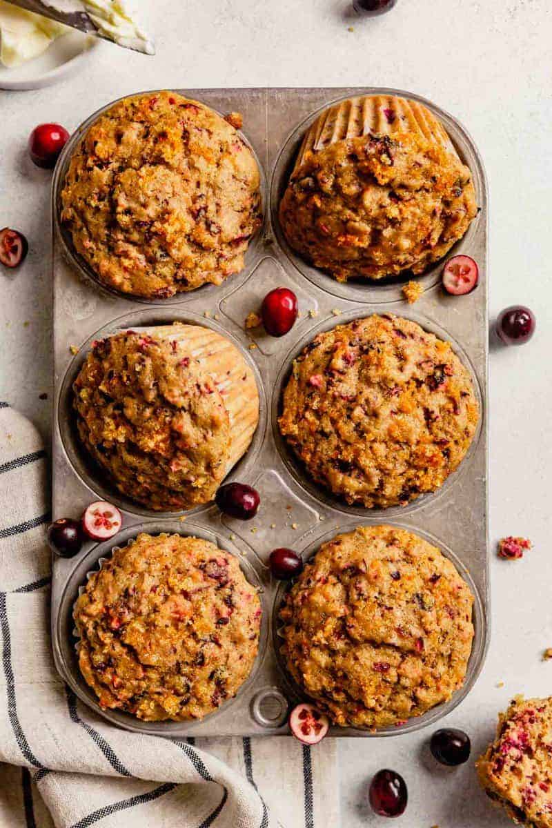 cranberry orange muffins in a muffin tin with cranberries scattered around