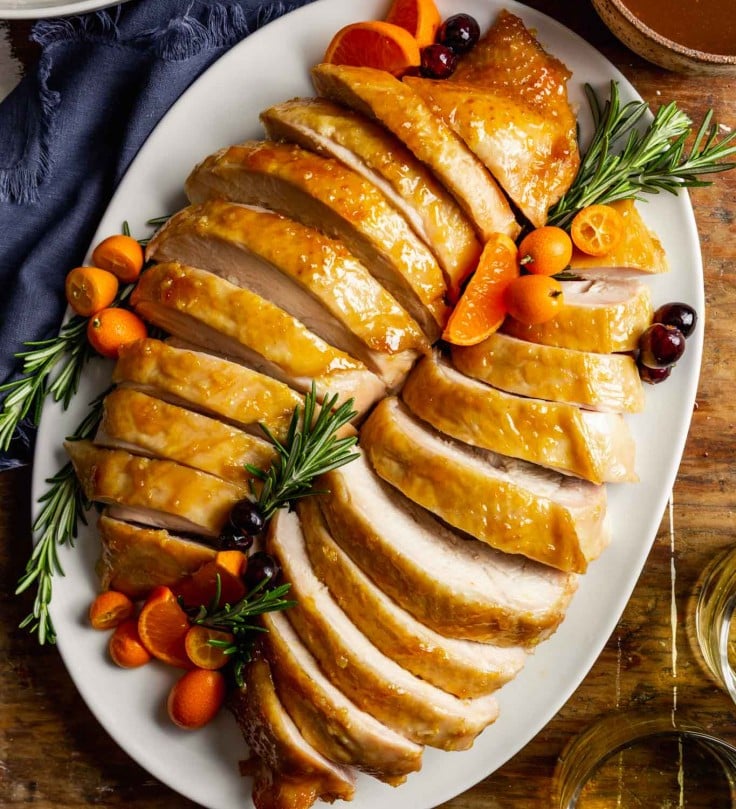 sliced turkey breast on a large white oval set on a wooden table