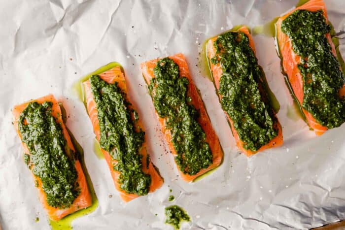 fillets of salmon on a foil-lined baking sheet topped with pesto