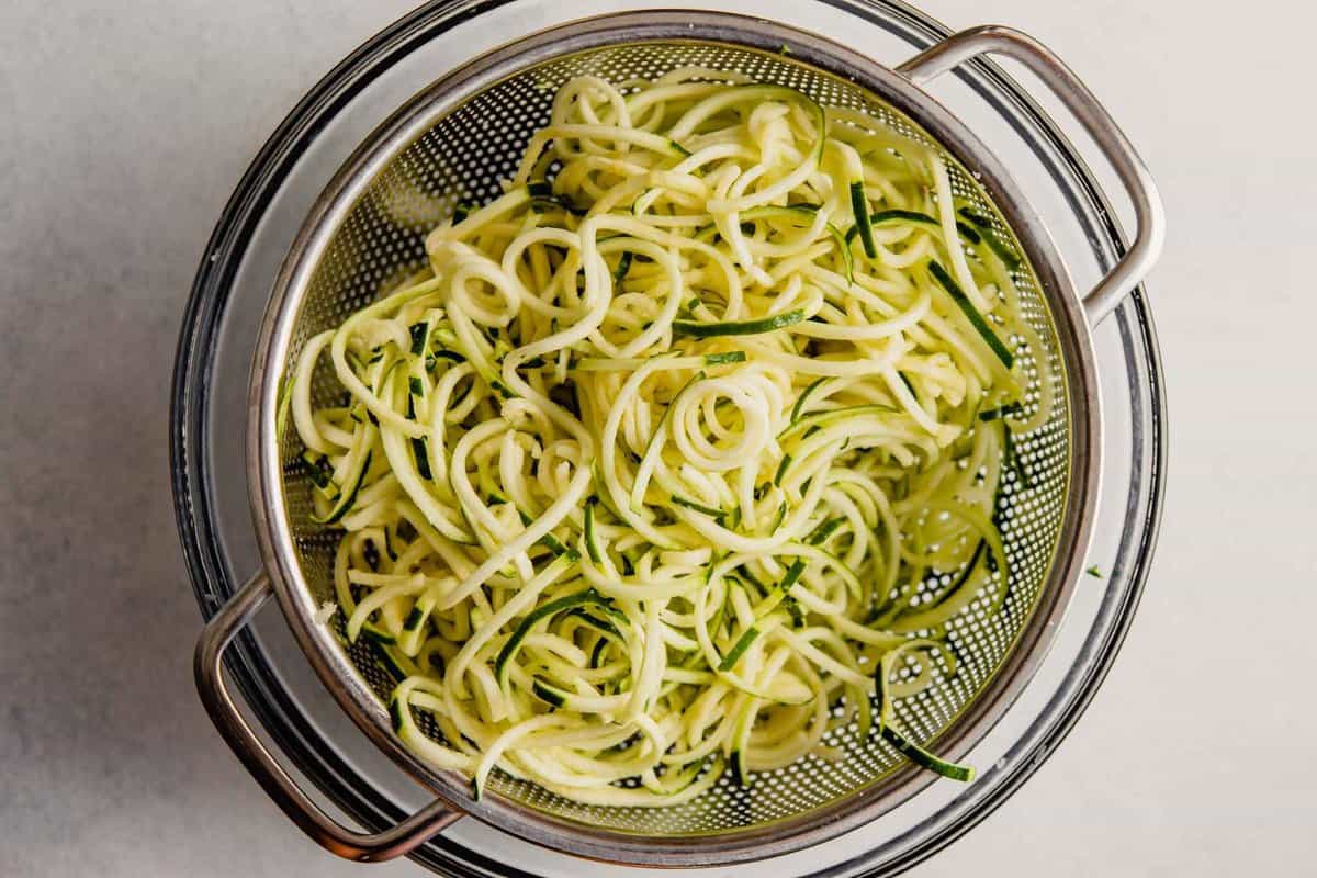 zucchini noodles in a colander set over a glass bowl