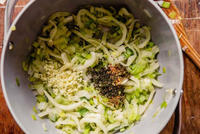 spices and herbs added to a pot of softened onions, leeks and fennel