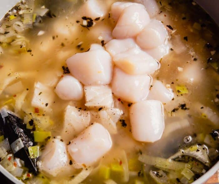 chunks of fish, scallops, mussels and shrimp in a large pot of broth