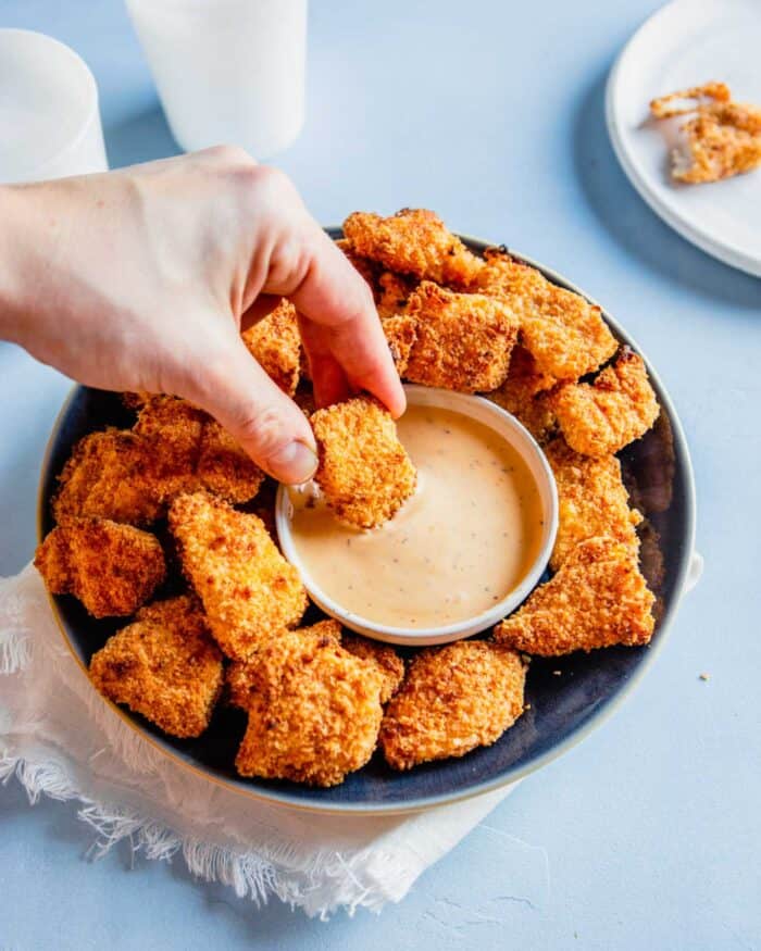 two fingers dipping a piece of crispy chicken in a creamy orange sauce