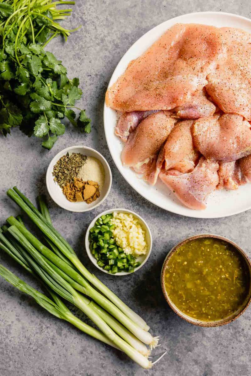 raw chicken, spices, herbs, salsa verde, and scallions arranges on a table top