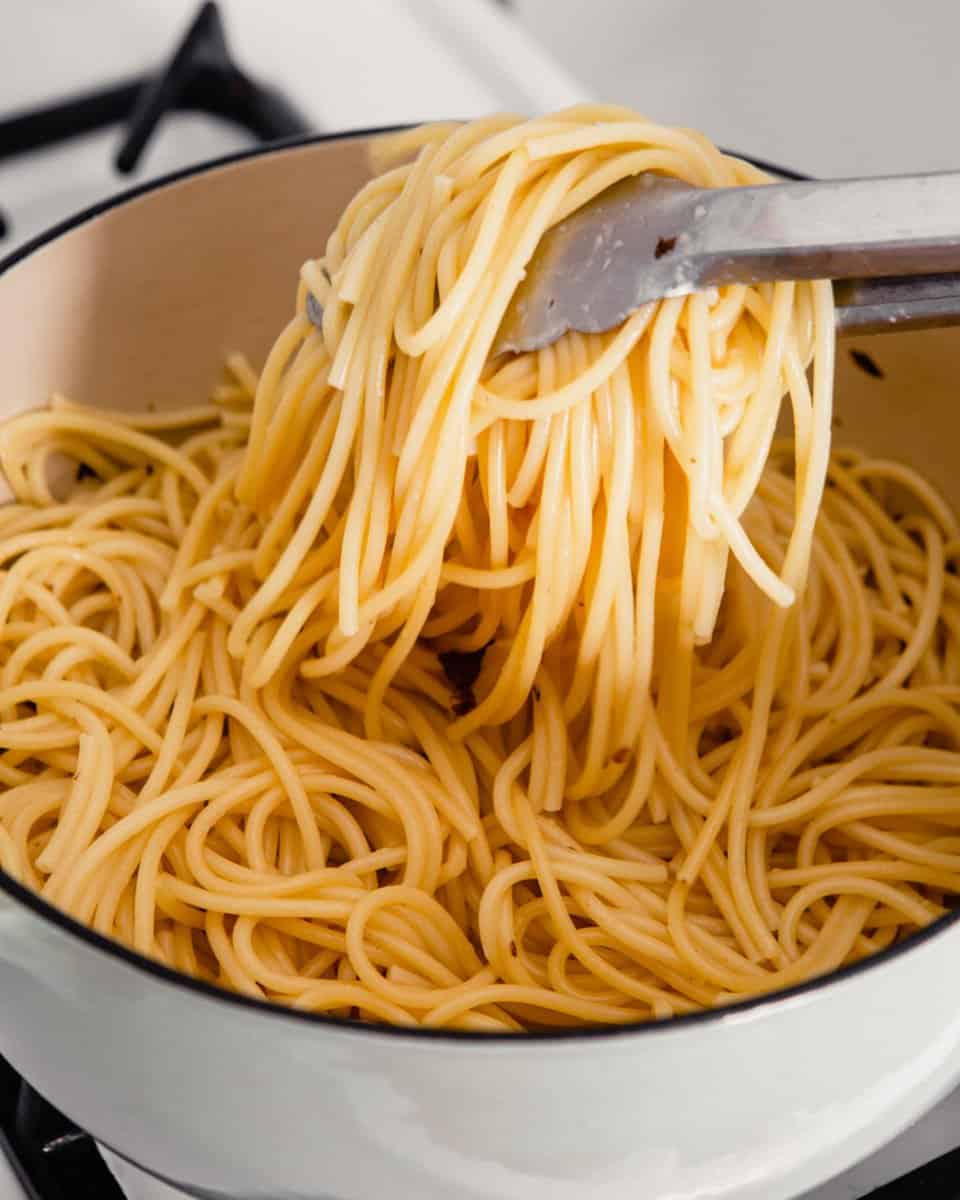 cooked spaghetti getting tossed with tongs in a dutch oven