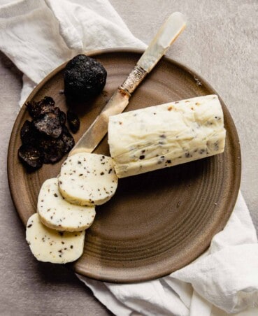 a log of truffle butter set on a brown plate with a few slices cut out of it and laying in a fan