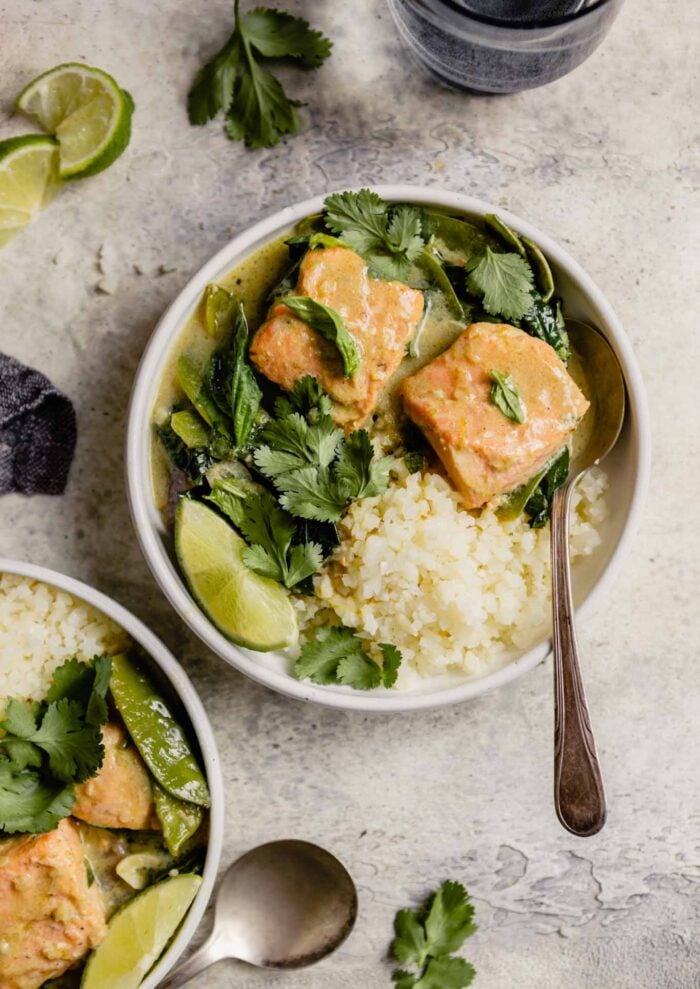white bowl filled with cauliflower rice, large chunks of salmon and green curry sauce