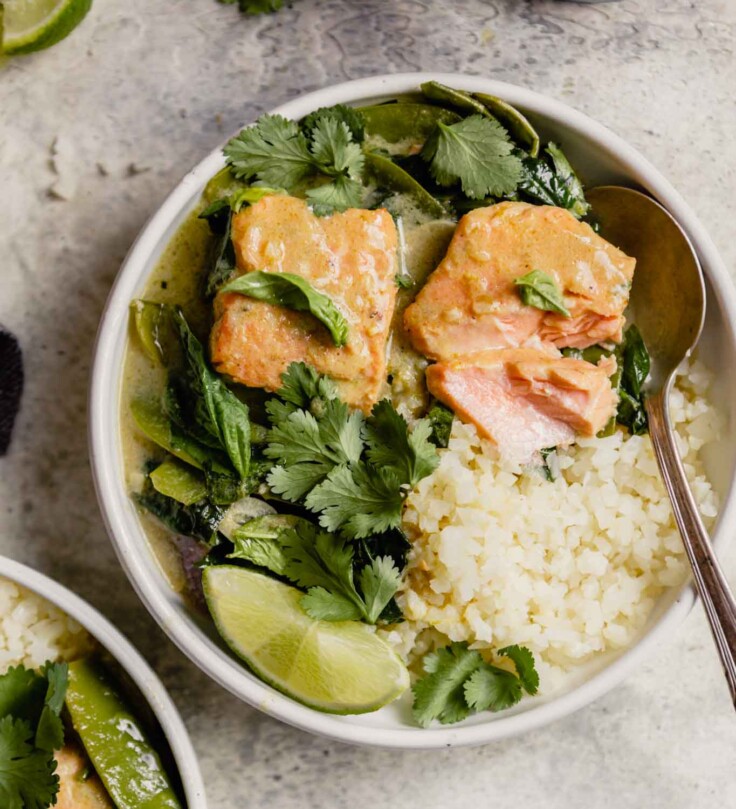 white bowl filled with cauliflower rice, large chunks of salmon and green curry sauce